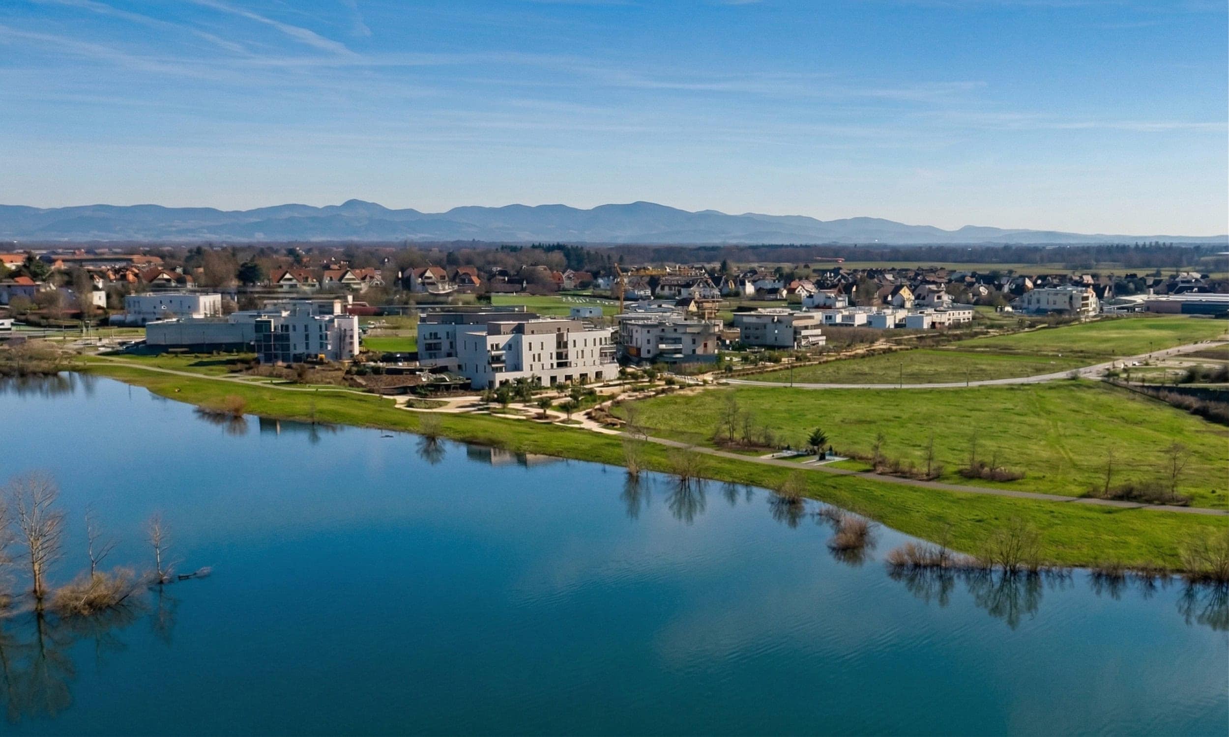 Quartier de logements durables au bord d’un lac en Alsace, avec les Vosges en arrière-plan